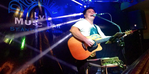 Darran Cooper performing live with an acoustic guitar on stage 